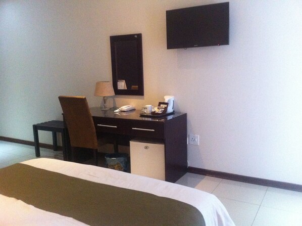 A hotel room with a bed, a desk, a chair, a TV, and a small cabinet. - Emerald Hotel (Gaborone)