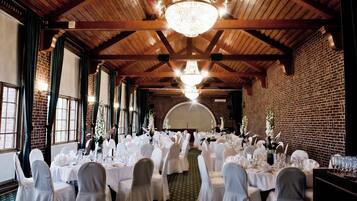 Un salón de banquetes con techos altos de madera y paredes de ladrillo, equipado con candelabros y mesas dispuestas para un evento formal.
