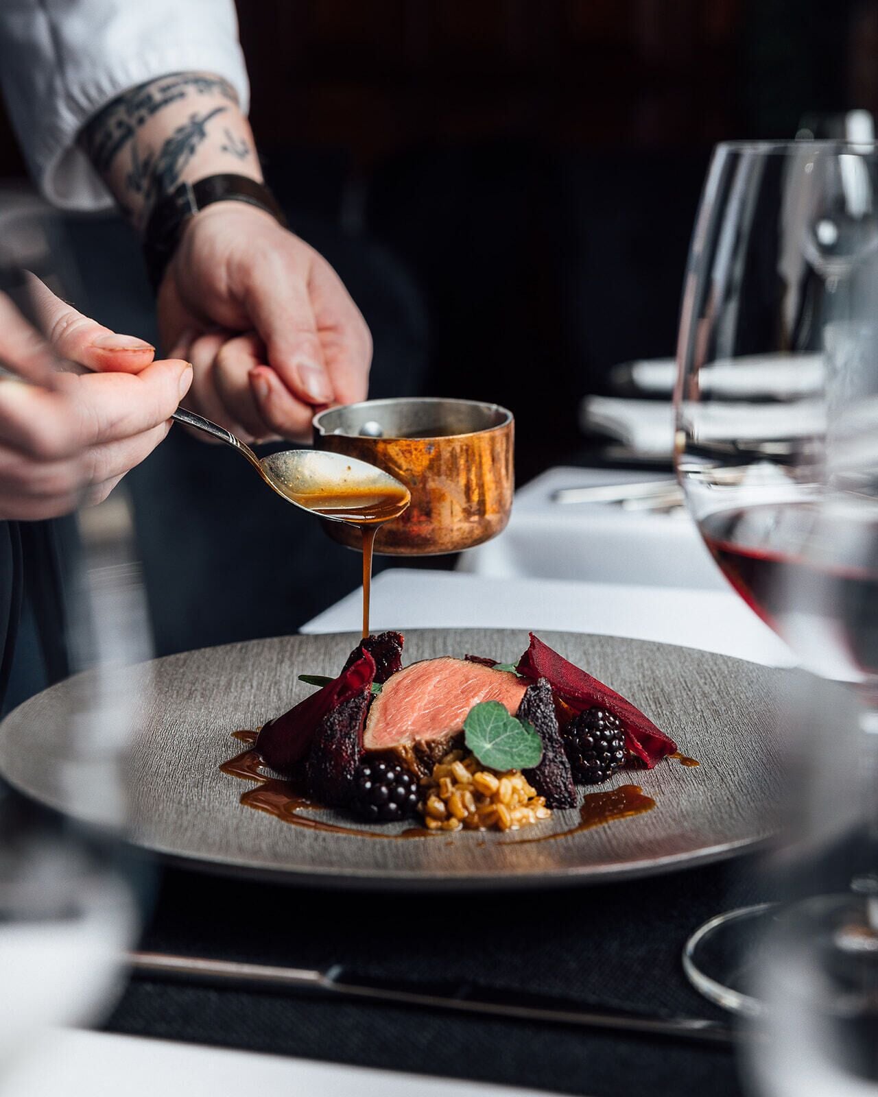 A chef pouring sauce over a dish with various ingredients.