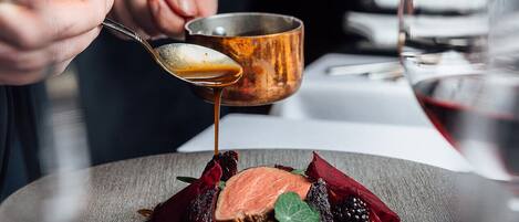 A chef pouring sauce over a dish with various ingredients.