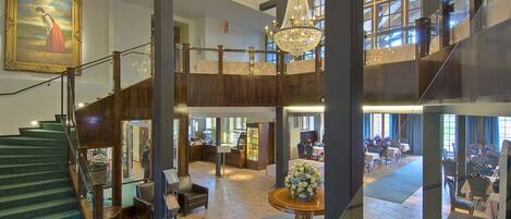 A spacious lobby with a grand staircase, a chandelier, and a large painting.