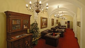 A grand hallway with a red carpet, leather sofas, a wooden bookcase, and a large chandelier. - Hotelli Vanajanlinna (Hameenlinna)