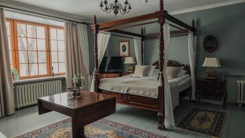 A four-poster bed, a chandelier, a television, and a radiator in a room with a large window and a patterned rug.
