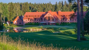 A large, multi-story building with a red roof, surrounded by a well-maintained golf course and a forested area. - Hotelli Vanajanlinna (Hameenlinna)