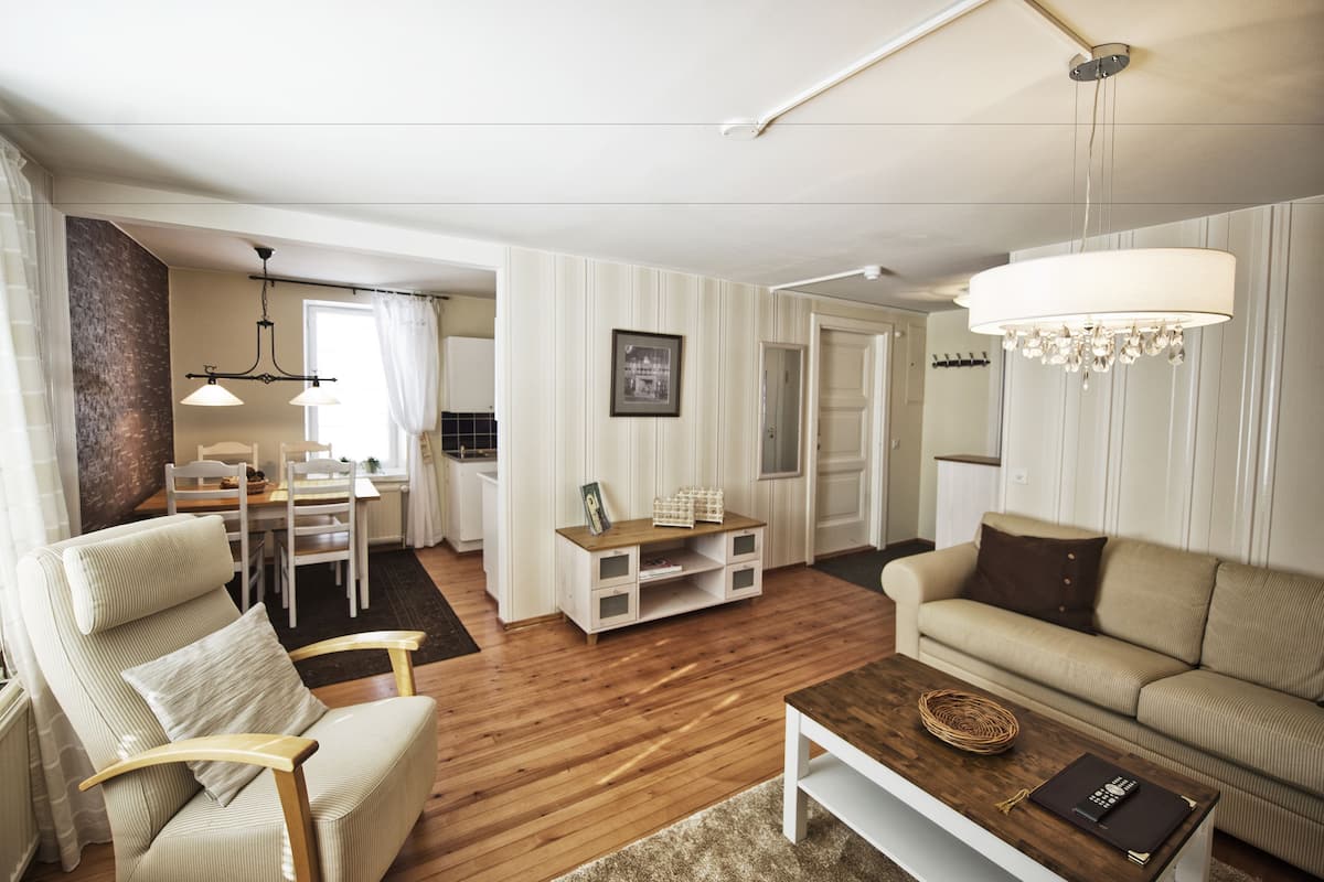 Een woonkamer met een bank, fauteuil, houten bijzettafeltje en een eethoek met tafel en stoelen.
