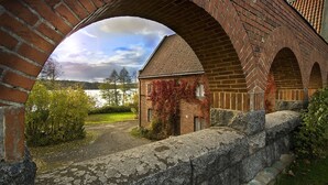 A brick bridge with an arched opening, a stone wall, and a building with ivy. - Hotelli Vanajanlinna (Hameenlinna)