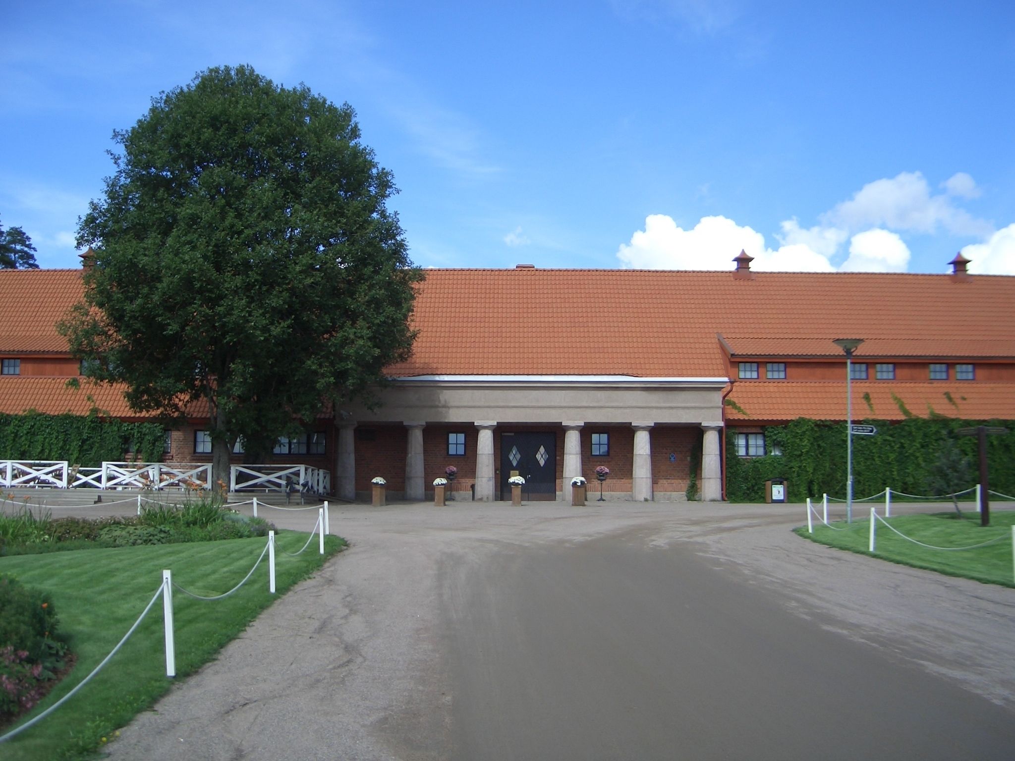 En bygning med røde tegltag, et stort træ foran og en belagt indgang.