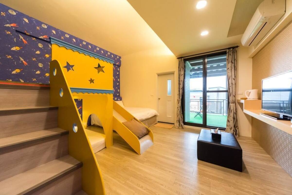 A room with a wooden staircase, a bed, a small table, and a TV.