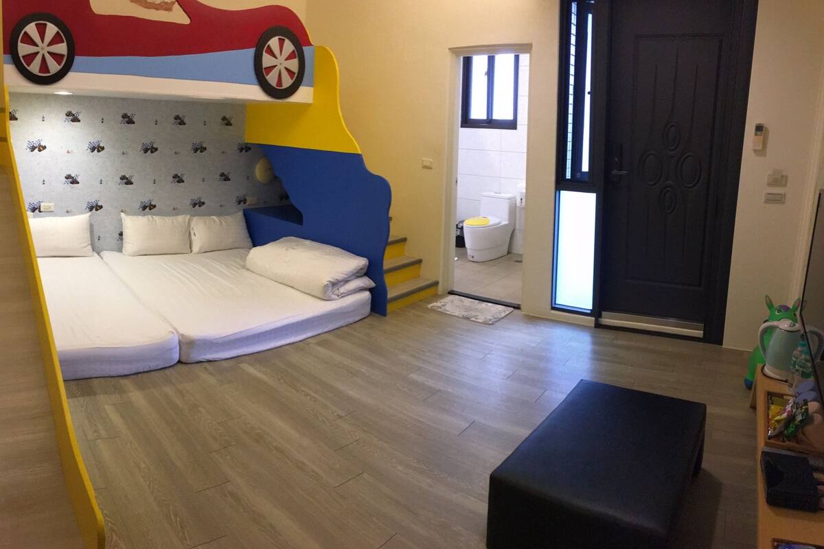 A room with a bed featuring a colorful headboard, a wooden floor, a black bench, and a small table with a toy.