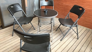 Una mesa redonda pequeña con dos sillas negras, una taza de café y una ventana con vista a edificios.