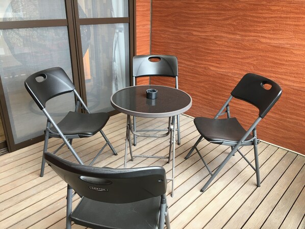 Una mesa redonda pequeña con dos sillas negras, una taza de café y una ventana con vista a edificios.