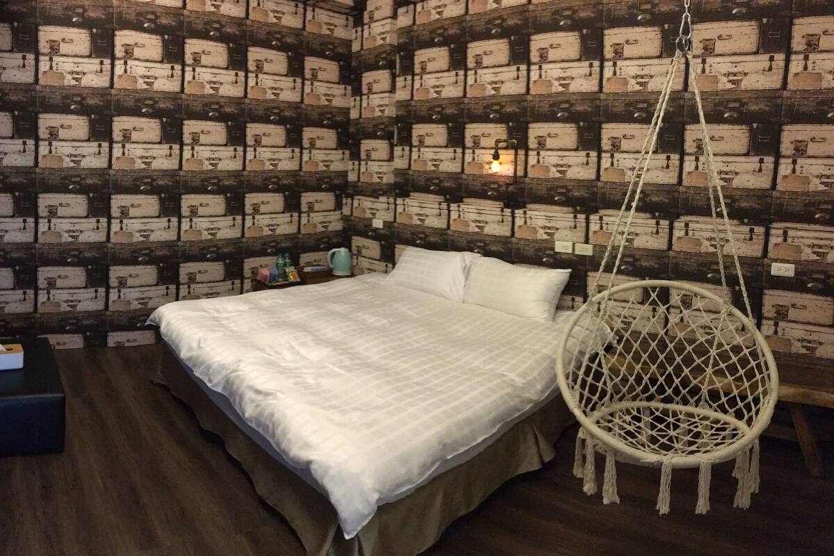 A bedroom with a bed, a hanging chair, and a wall with a patterned design.
