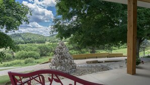 A red bench under a covered area with a view of a forested landscape and a pile of branches. - Cabin and Private Basketball Gym, Hocking Hills (Logan)