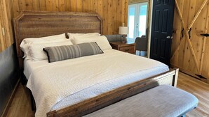 A wooden-paneled bedroom with a large bed, a bedside table with a lamp, and a door with a cross-brace design. - Cabin and Private Basketball Gym, Hocking Hills (Logan)
