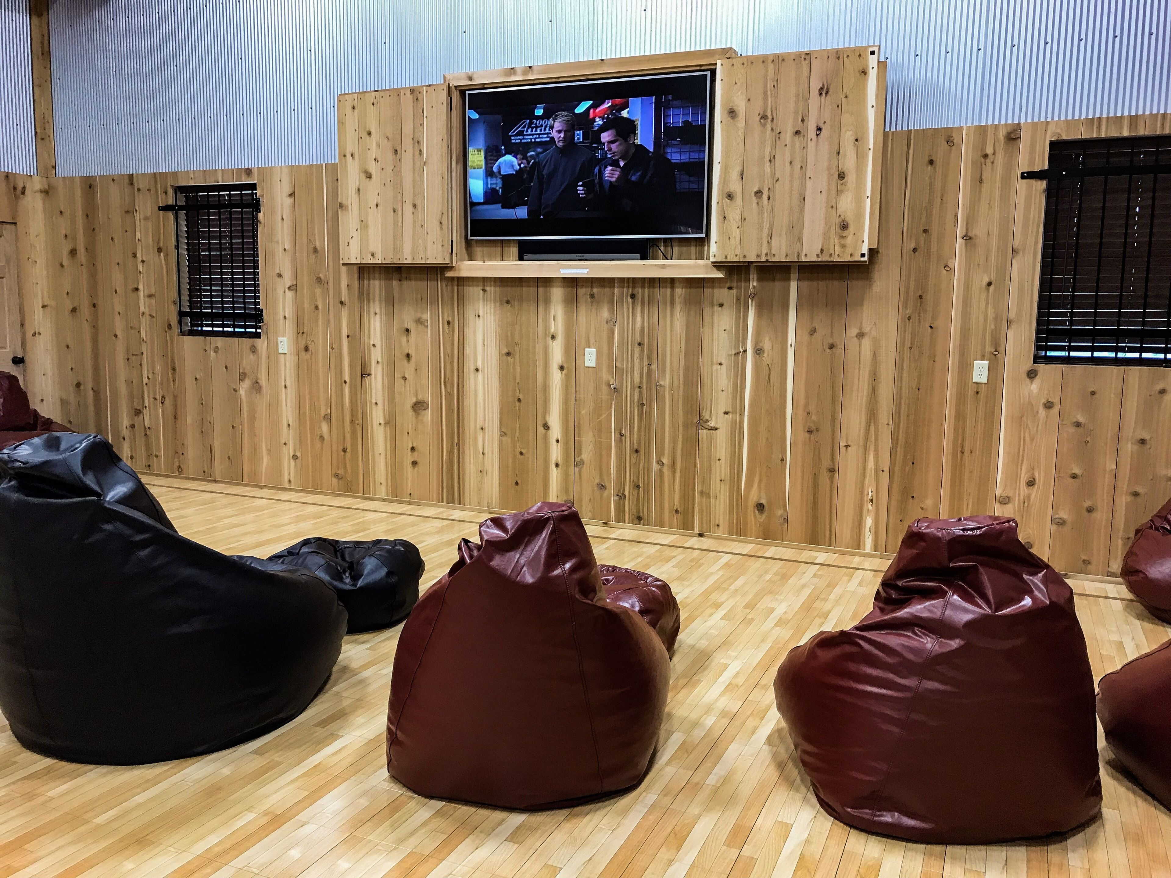 Una habitación con pared de madera, un televisor montado y varios puffs.