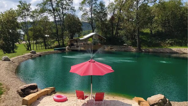 A circular pond with a red umbrella and two red chairs on a sandy area. - Cabin and Private Basketball Gym, Hocking Hills (Logan)
