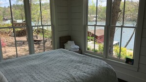 A bedroom with a large window, a bed, and a view of a lake and outdoor area.