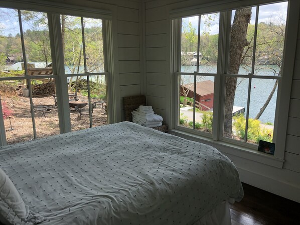Un dormitorio con un ventanal grande, una cama y vistas a un lago y zona exterior.