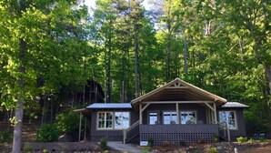 A cabin with a wooden exterior, a porch with chairs, and a stone pathway leading to the entrance.