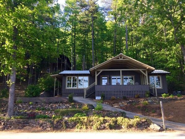 A cabin with a wooden exterior, a porch with chairs, and a stone pathway leading to the entrance.