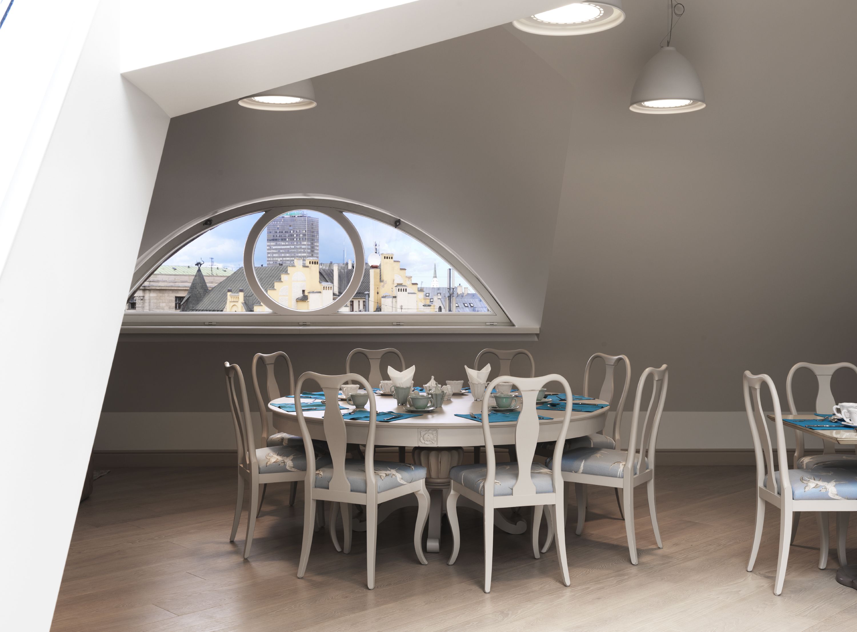 A dining area with a high ceiling, a large arched window, and a city view.