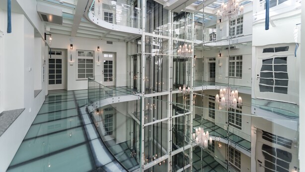 Un atrium à plusieurs niveaux, doté de rampes en verre, d’un escalier central et de lustres.