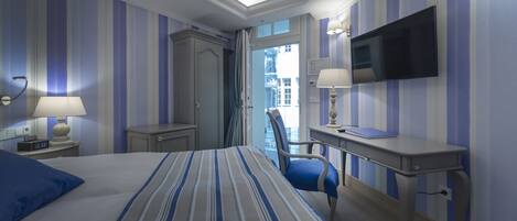 Habitación de hotel con una cama grande, un escritorio, una silla, un televisor y vistas a la ciudad.