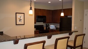 Una cocina con armarios de madera, microondas, estufa, refrigerador y una zona de bar con dos sillas.