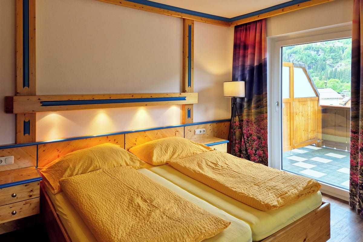 Une chambre avec deux lits, une tête de lit en bois, une lampe et une vue sur la verdure par une fenêtre.