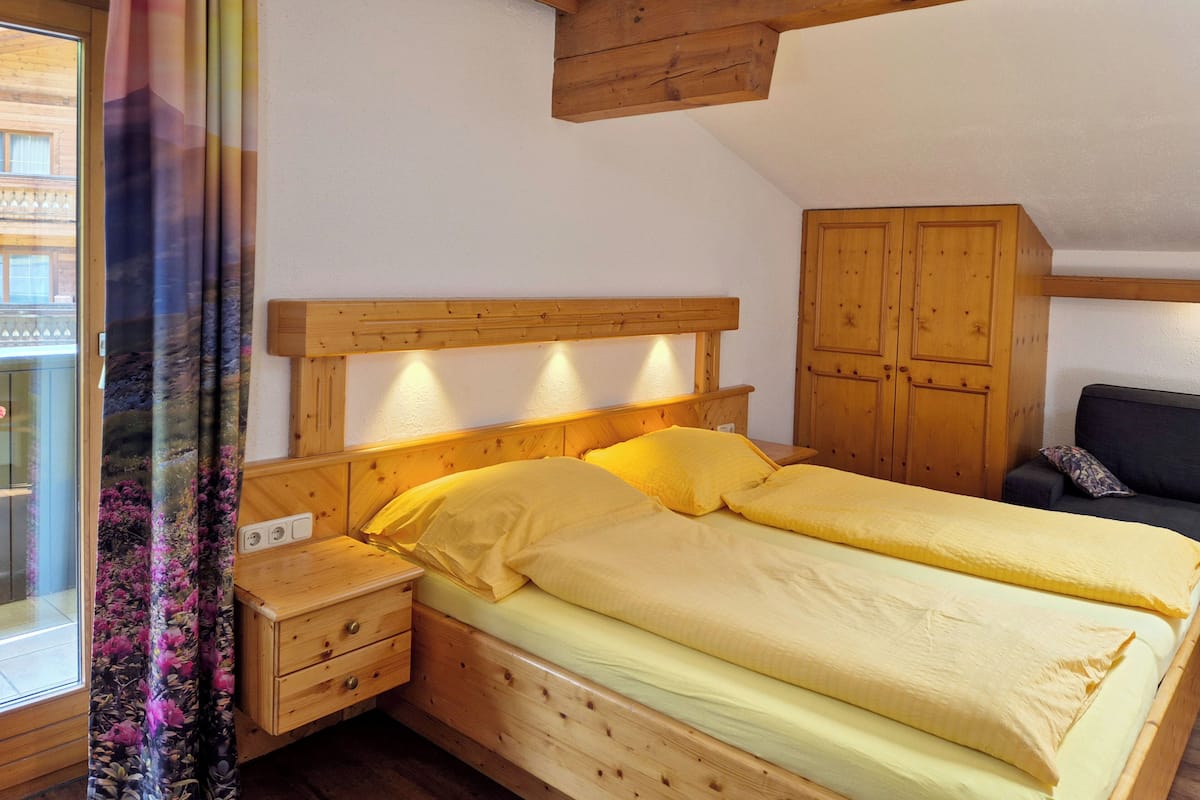 Un lit en bois avec deux oreillers et une table de chevet, une armoire en bois et une fenêtre avec des rideaux.