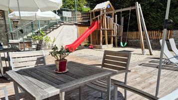 Relax on the outdoor patio with a wooden deck, shaded by umbrellas and surrounded by lush greenery.