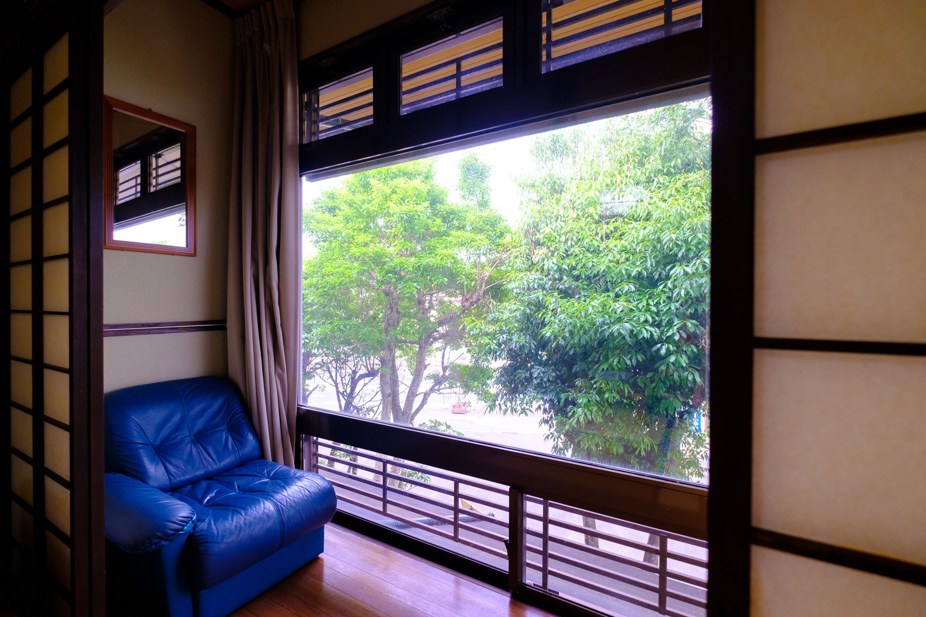 A room with a blue leather sofa, a large window with a view of trees, and traditional Japanese sliding doors.