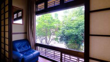 A room with a blue leather sofa, a large window with a view of trees, and traditional Japanese sliding doors.