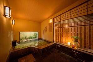 A traditional Japanese bath with a wooden ceiling, a window with a view of greenery, and a potted plant on the windowsill. - Good Stay Mizuho (Usa)