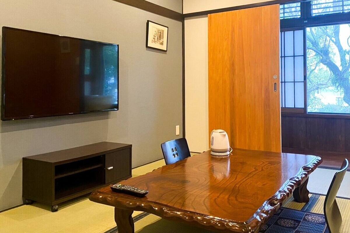 A traditional Japanese room with tatami flooring, a wooden table, a television, and a sliding door.