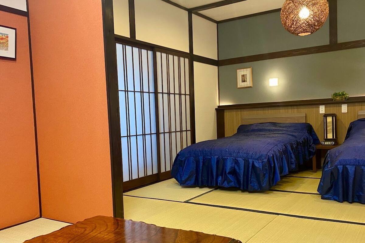 A traditional Japanese room with tatami flooring, two beds with blue bedding, a wooden table, and a shoji screen.