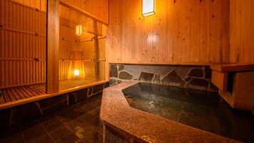 A wooden interior with a stone-lined hot tub and a wooden bench.