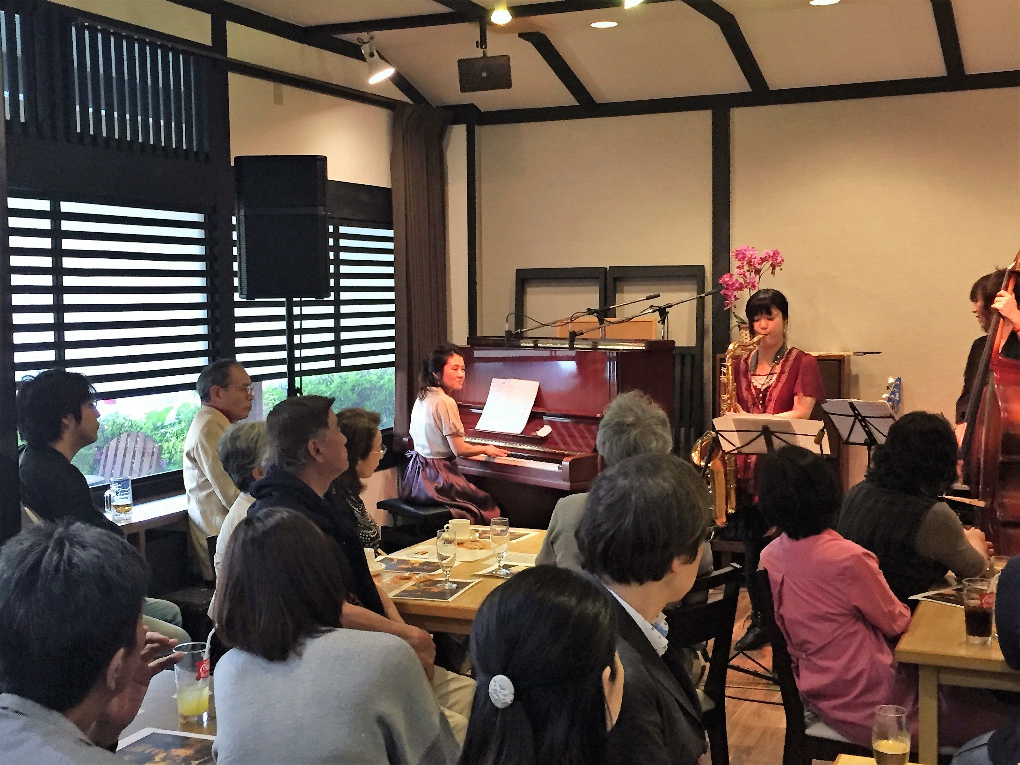 A room with a piano, a seated audience, and a speaker.