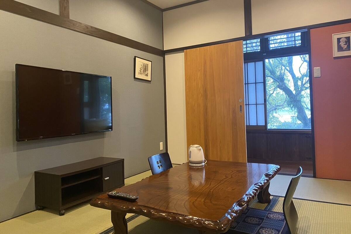 A conference room with a wooden table, chairs, a television, and a picture on the wall.