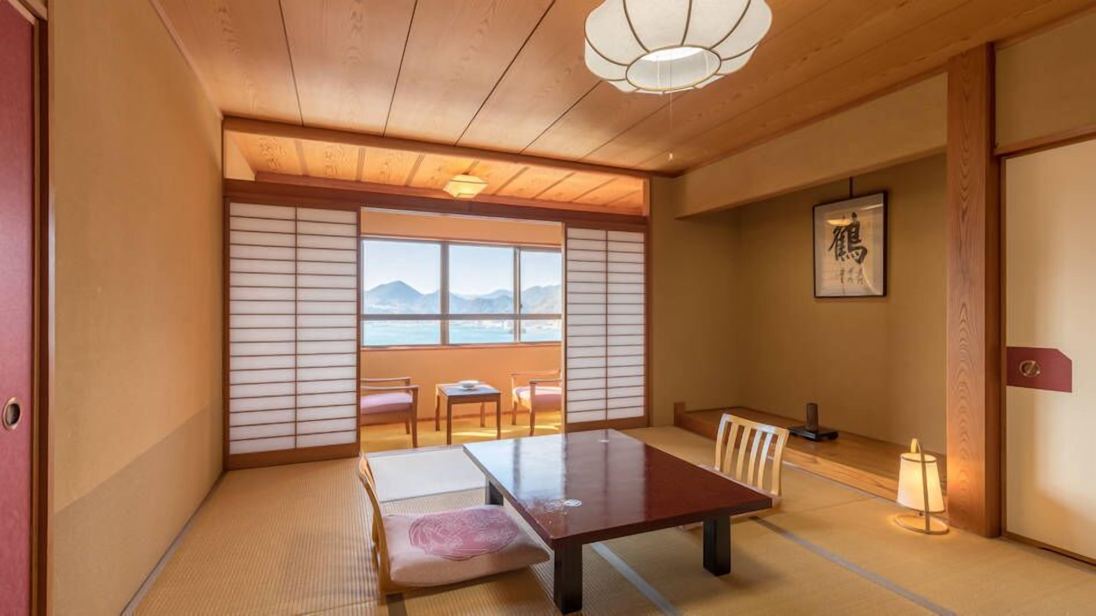 Ein traditioneller japanischer Raum mit Tatami-Böden, einem niedrigen Tisch, Stühlen, einer Schiebetür und Blick auf die Berge.