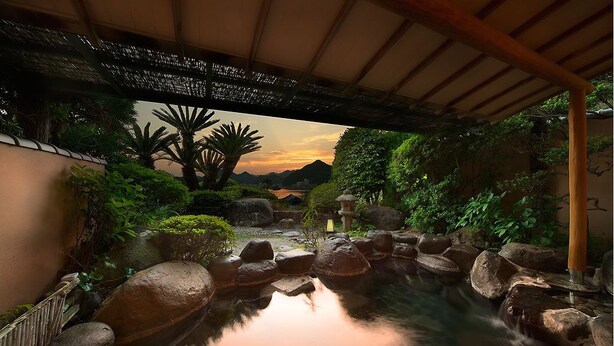 Un jardín tranquilo con fuente, rocas y abundante vegetación bajo una pérgola de madera.
