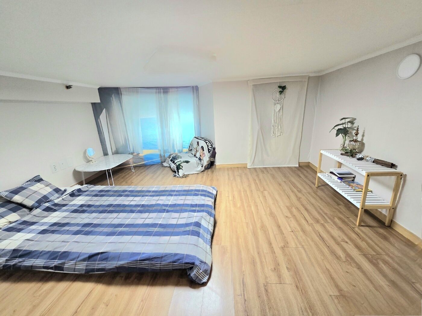 A bedroom with a bed, a desk, and a shelf with books and decorative items.