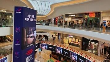 A multi-level shopping mall with a central atrium, escalators, and a large digital advertisement.