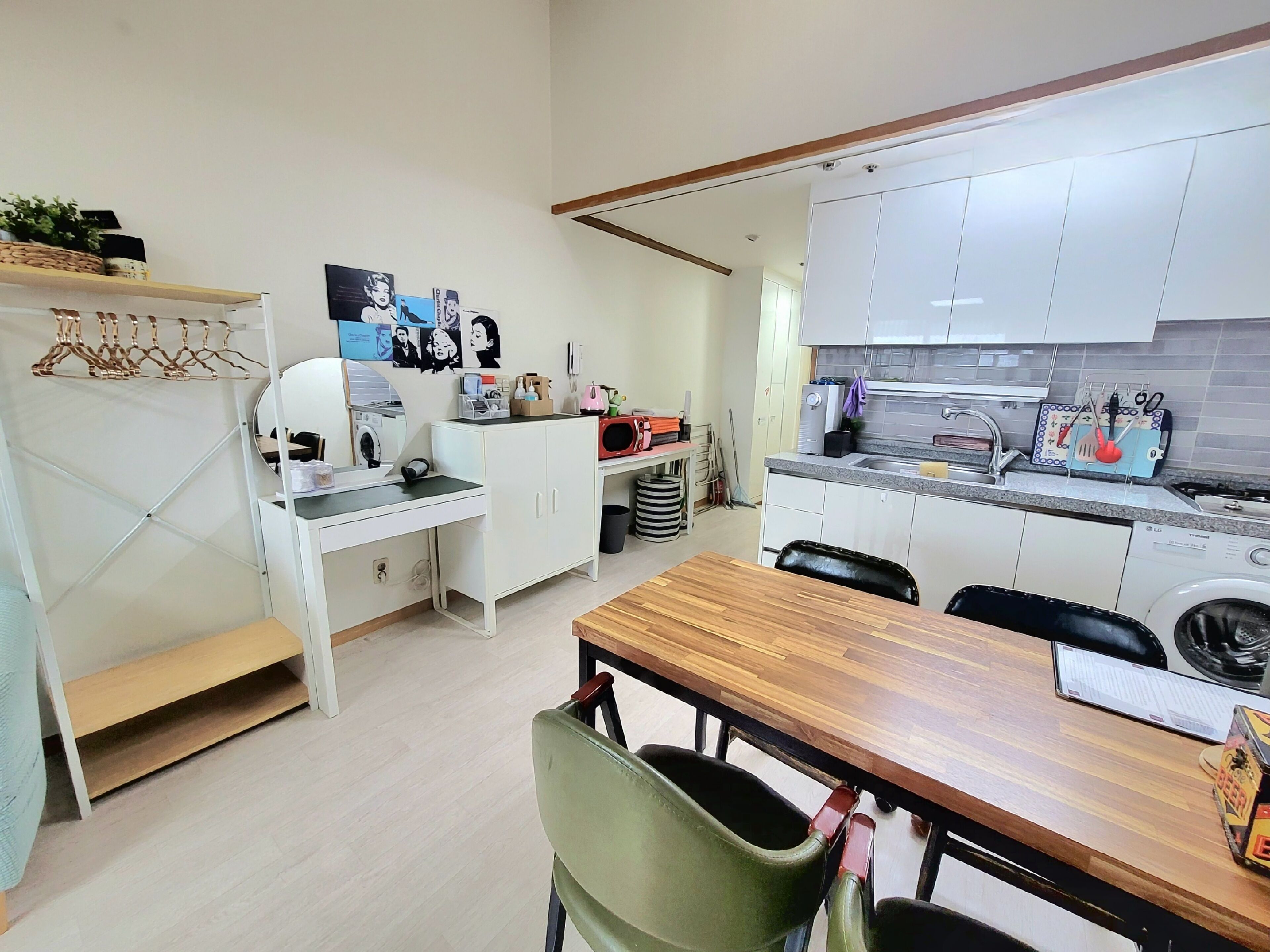 Une cuisine de taille réduite avec des meubles blancs, une table à manger en bois et un lave-linge.