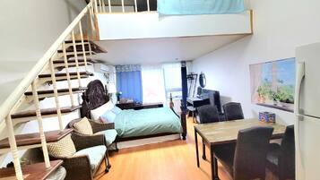 A loft-style bedroom with a staircase, a bed, a desk, and a dining area.