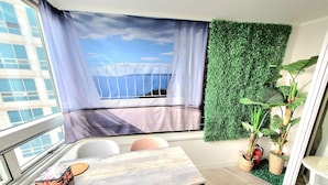 Un balcón con vista al mar, una mesa con sillas y una pared verde con plantas.