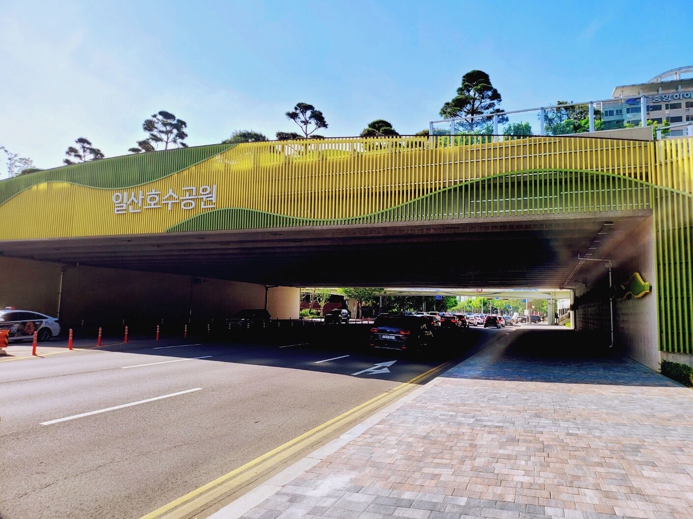 Une passerelle piétonne couverte, dotée d’un toit incurvé, d’une rambarde jaune et d’une signalisation dans une langue étrangère.