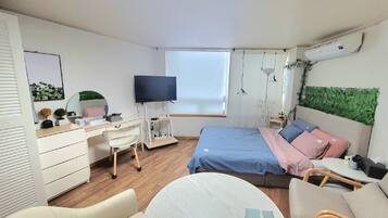Un dormitorio con cama, escritorio, silla, televisor y ventana.