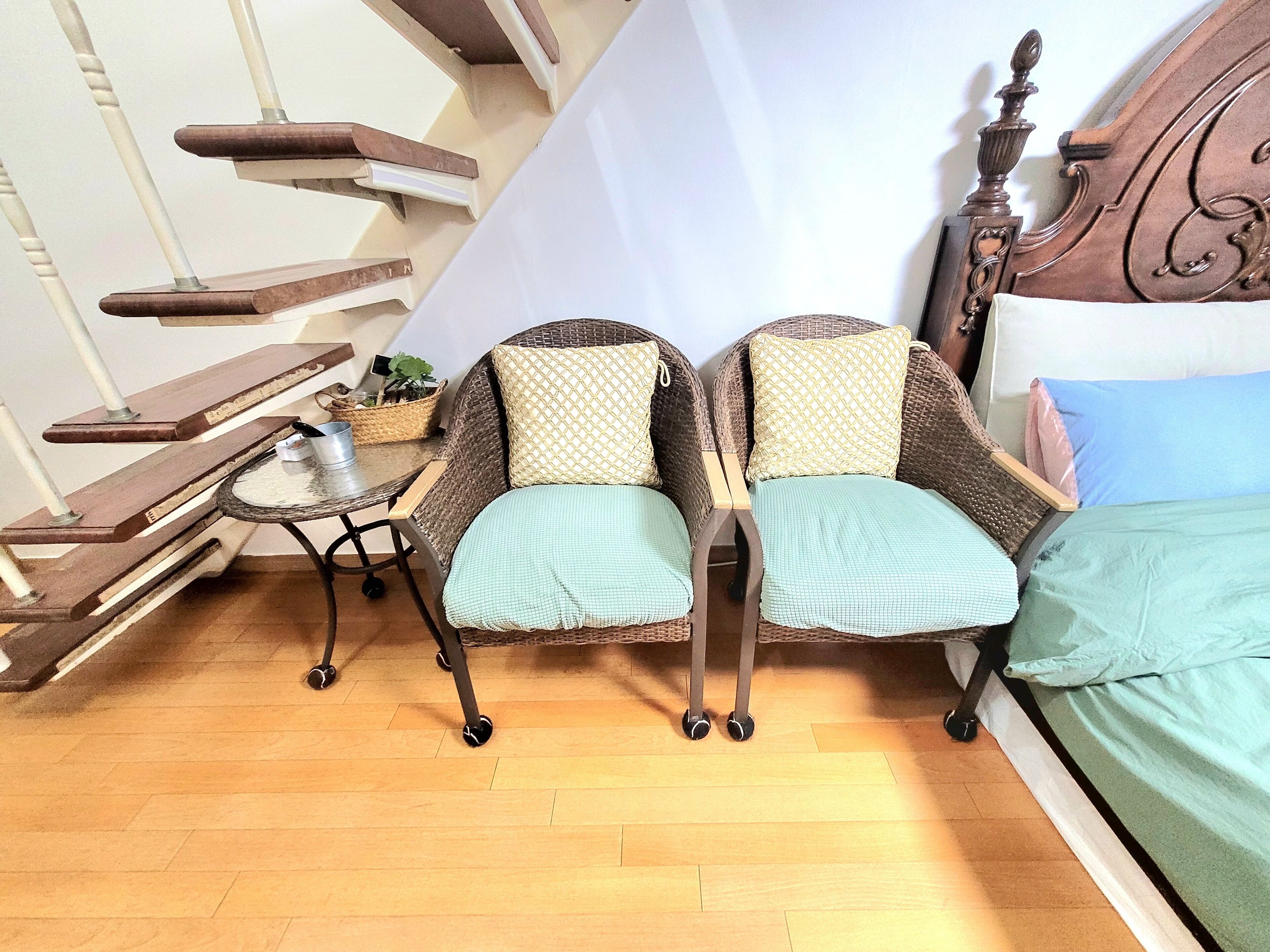 Une pièce comprenant un lit, deux fauteuils en osier, une petite table avec une plante et un escalier.