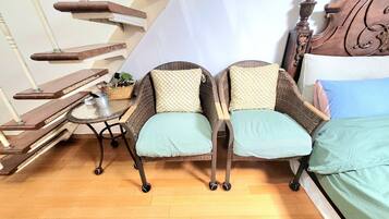 Une pièce comprenant un lit, deux fauteuils en osier, une petite table avec une plante et un escalier.
